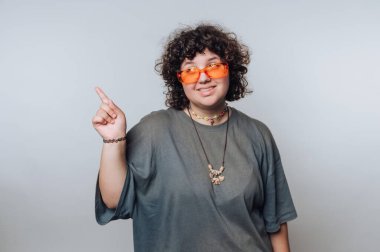 Açık arkaplanda turuncu güneş gözlüğü takan kıvırcık saçlı genç kadının portresi