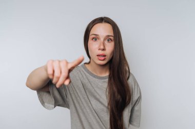 Gri giyinmiş genç bir kadının portresi, arka planda kamera dışı bir şeye işaret ederken ürkmüş görünüyor.