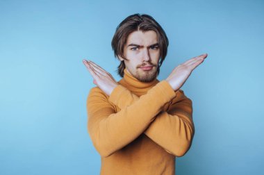 Genç bir adamın portresi, kollarını kavuşturup, mavi arka plandaki güçlü bakış açısını vurgulayan yoğun bir ifade sunar.