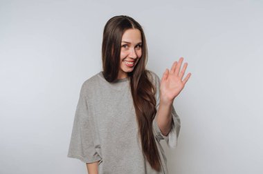 Dost canlısı genç bir kadının portresi ışık arka planda sıcak bir gülümsemeyle el sallıyor.