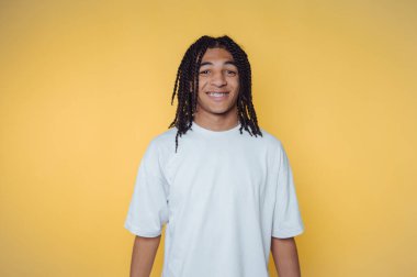 Saçları örgülü genç bir adamın portresi sarı arka planda dururken sıcacık gülümsüyor.