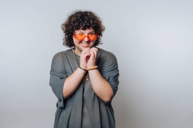 Şaşırmış kıvırcık saçlı genç bir kadının portresi portre şeklinde çekiliyor, açık arkaplanda neşeli bir ifade sergiliyor.