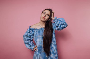 Kafası karışmış genç bir kadının portresi. Pembe arka planda mavi kareli bir elbise giyiyor.