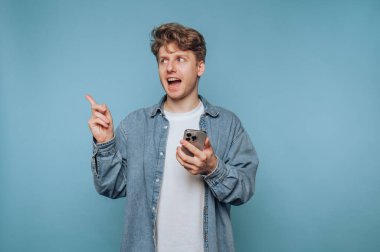 Genç bir adamın portresi parlak bir fikri ifade eder, akıllı telefonuyla meşgul olurken, açık mavi arkaplanı göstererek.