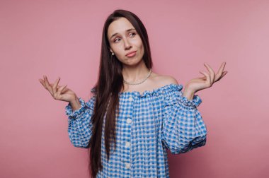 Mavi kareli elbiseli genç bir kadının portresi açık ellerle kafası karışmış görünüyor, pembe arka plandaki sorgulamayı temsil ediyor.