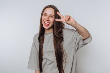 Genç bir kadının portresi bir barış işaretiyle neşeli bir şekilde poz veriyor, ışık arka planında neşe ve güven sergiliyor