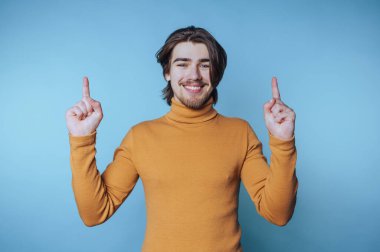 Parlak bir gülümsemeyle genç bir adamın portresi mavi arka plandaki neşe ve pozitifliği simgeleyen ellerini yukarı kaldırır.