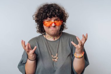 Şaşırmış kıvırcık saçlı genç bir kadının portresi açık arkaplandaki el hareketleriyle duygularını ifade eder.