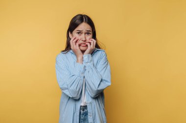 Genç kızın portresi endişeli bir yüz ifadesi sergiliyor. Sarı arka planda bir anksiyete anı yakalıyor.