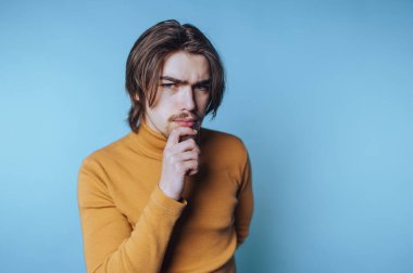 Rahat bir balıkçı yaka giyen genç bir adamın portresi mavi arka planda tefekkürle poz veriyor.