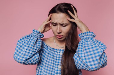 Genç bir kadının portresi sıkıntılı görünüyor, başını tutuyor ve pembe arka planda acı dolu bir ifade sergiliyor.