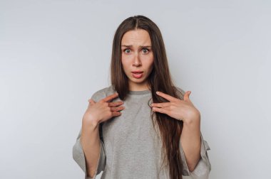 Gri gömlekli, kafası karışmış genç bir kadının portresi belirsiz görünüyor. Göğsünde bir el ve arka planda sorgulama ifadesi var.