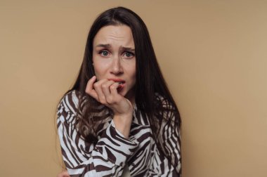 Tırnaklarını gergin bir şekilde yiyen genç bir kadının portresi sakin sarı arka planda endişelerini açığa çıkarıyor.