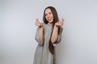 Genç bir kadının portresi jestlerle oynar, parmakları açık arkaplanda küçük kalp şekilleri yaratır