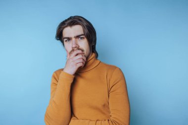 Genç bir adamın portresi, mavi arka planda iç gözlem duygusunu göstererek, çenesini derin düşüncelere daldırır.