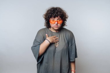 Şaşırmış kıvırcık saçlı genç bir kadının portresi. Elini kalbine koyuyor. Hafif arka planda samimiyet hissi veriyor.