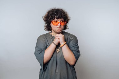 Açık arkaplanda dudaklarını ısırırken gergin bir ifadeyle şaşırmış kıvırcık saçlı genç bir kadının portresi