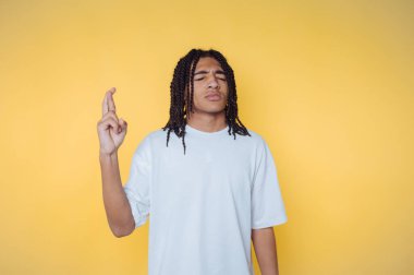 Sarı arka planda beyaz bir gömlek giymiş, parmakları çapraz genç adam portresi.