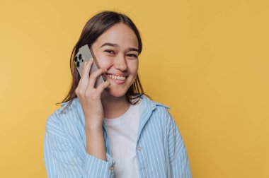 Neşeli genç kızın portresi sarı arka planda yapılan bir telefon görüşmesinden hoşlanıyor.