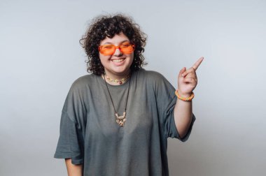 Turuncu güneş gözlüğü takarken geniş gülümseyen kıvırcık saçlı genç kadının portresi, pozitifliği ve ışık arka planında sıcaklığı somutlaştırıyor.