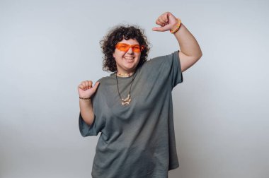 Şaşırmış kıvırcık saçlı genç bir kadının portresi açık arkaplanda dans ederken kendine güven ve neşe saçar.