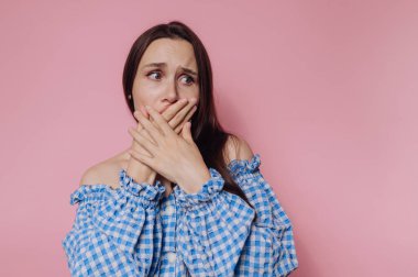 Genç bir kadının portresi, pembe arka planda endişeli bir bakışla ağzını kapatırken endişe ve endişe ifade eder.