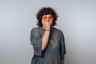 Şaşırmış kıvırcık saçlı genç bir kadının portresi endişeli bir bakışla, açık arkaplanda dudaklarını düşünceyle kaplıyor.