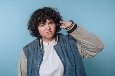 Genç bir kadının portresi, mavi arka planda belirsizlik ve tefekküre işaret eden küçük bir jest sergiliyor.