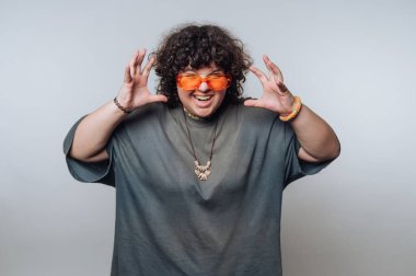 Şaşırmış kıvırcık saçlı genç kadının portresi açık arkaplanda neşeli bir şekilde el kaldırıyor.