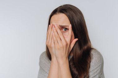 Genç, korkusuz kadının portresi elleriyle yüzünü örtüyor. Kırılganlığını ve iç mücadelesini ışık arka planında gösteriyor.