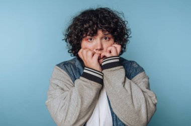 Genç bir kadının portresi, elleri mavi arka planda yüzünü kaplayan şaşırtıcı bir ifade sergiliyor.