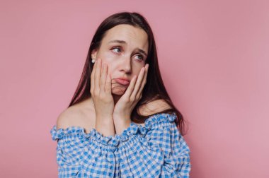Genç bir kadının portresi, yüzünü tutarken hüzünlü bir ifade sergiliyor, pembe arka planda endişe ve endişeyi ifade ediyor