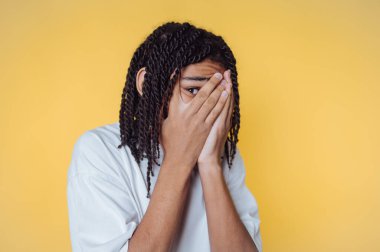 Genç adamın portresi elleriyle yüzünü gizliyor, sarı arka planda duygularının karışımını sergiliyor.