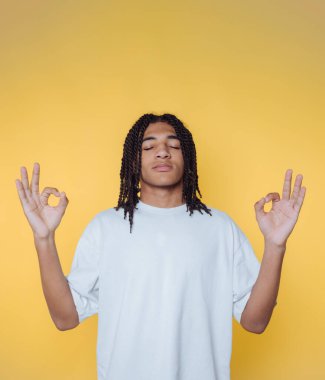 Genç bir adamın portresi huzur içinde meditasyon yapıyor. Sarı arka planda iç sakinliğini sergiliyor.