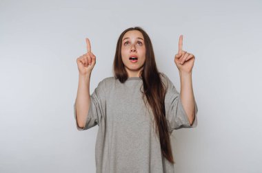 Gri gömlekli genç bir kadının portresi açık arkaplandaki hayret verici ifadesini göstererek şaşkınlığını gösteriyor.