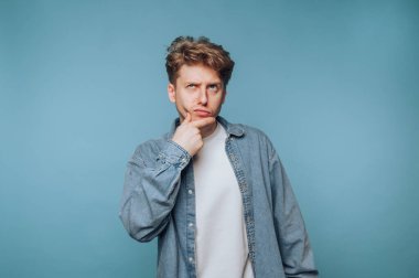 Genç adamın portresi elleri çenesinde, açık mavi arka planda derin derin düşünürken görülüyor.