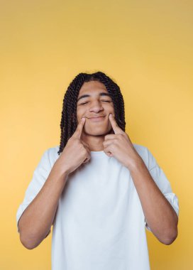 Genç adamın portresi neşeli bir şekilde gülümserken parmakları sarı arka planda bir jest yapıyor.