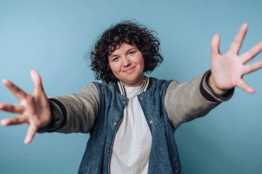 Genç bir kadının portresi mavi arka planda dostça bir jest yaparak kollarını uzatır.