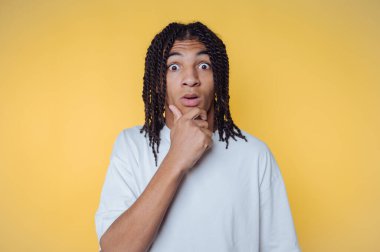 Genç adamın portresi, çenesini hayret verici bir ifadeyle tutarak, sarı arka planda merak ve düşünceliliği yansıtıyor.