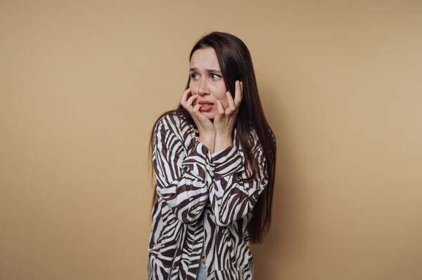 portrait of young woman displays a distressed expression, holding her face in shock, conveying emotions of fear and anxiety on calm yellow background