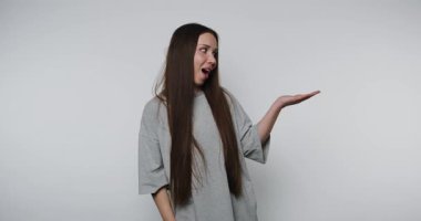 Uzun saçlı bir kadın kafa karışıklığı sergiler, beyaz arka planda neşeli hareketlerle duygularını canlı bir şekilde ifade eder.