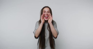 Neşeli genç bir kadın beyaz arka planda kameraya bağırırken geniş bir şekilde gülümsüyor.