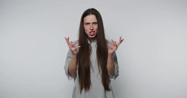 Uzun saçlı bir kadın hayal kırıklığı yaşıyor. Yumruklarını sıkarak somurtuyor. Beyaz arka planda can sıkıntısını yansıtıyor.