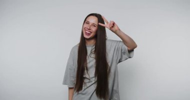 Genç oyuncu kadın beyaz arka planda neşeli ve kaygısız kişiliğini gösterirken barış işareti yapıyor.