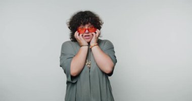 Genç kıvırcık kadın kafalarını tutuyor, saf duygularını sergiliyor ve beyaz arka planda hayal kırıklığının özünü yakalıyor.