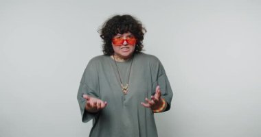 Genç kıvırcık kadın hayal kırıklığına uğramış duygularını sergiliyor, yumruklar oluşturuyor ve beyaz arka planda günlük giysiler giyiyor.