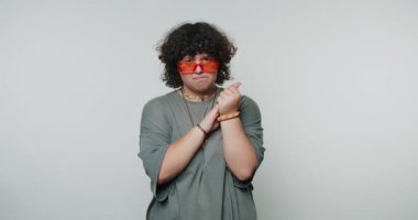 Kırmızı gözlüklü genç kıvırcık kadın düşünceli bir duruş sergiliyor, tefekkürün temaları, beyaz arka planda yansıma.