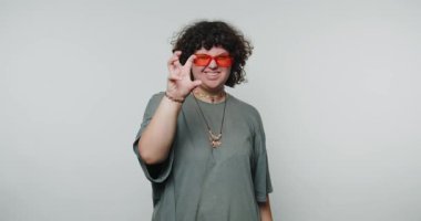 Büyük ölçekli neon gözlüklü genç kıvırcık kadın neşe saçıyor. Beyaz arka planda neşeli duygular ve enerjik bir enerji sergiliyor.