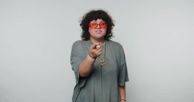 Odaklanan kadın, neon güneş gözlüğü takarken kararlı bir hareket sergiliyor, özgüveni yansıtıyor ve beyaz arka planda kararlılık gösteriyor