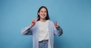 Kendine güvenen genç bir kız neşeli bir gülümsemeyle barış işareti sergiliyor. Mavi arka planda pozitifliği ve gençliği temsil ediyor.